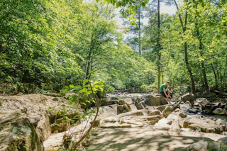Someone climbs over rocks along the water on the Duke Forest Trail.