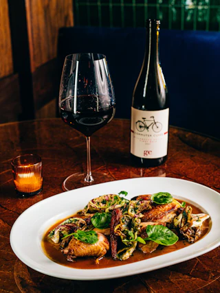 A glass of red wine sits full next to its bottle overlooking a chicken dish at Nana's in Durham.