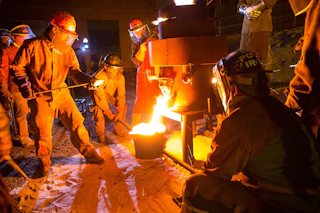 Iron workers in protective suits and helmets gather around a fire.