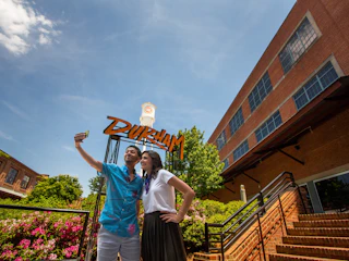 A couple poses for a selfie in front of the Durham sign at American Tobacco Campus.