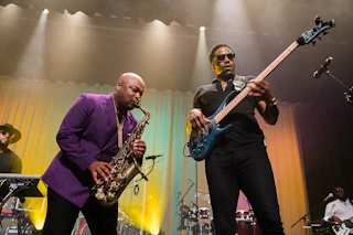 Two musicians performing on stage lit by yellow and green stage lights.