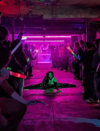 A performer dances under pink light between rows of people at Club Era in Durham, NC.