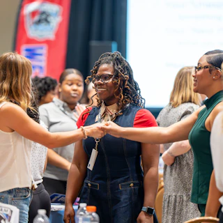 Women shake hands and smile at a conference in Durham, NC.