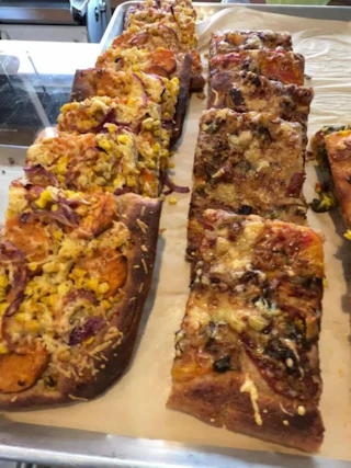 Rows of focaccia pizzas with assorted vegetable, cheese and meat toppings at Loaf